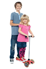 Image showing Brother holding her sister as she rides her toy scooter