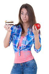 Image showing Girl in doubt with an apple and a cake