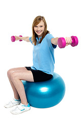 Image showing Girl sitting on pilates ball and doing dumbbells