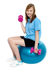 Image showing Pretty teen seated on a blue pilate ball doing dumbbells