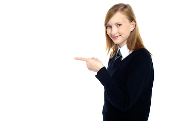 Image showing Pretty schoolgirl pointing towards copy space area
