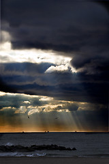 Image showing Sunbeams emanating through clouds above the ocean 