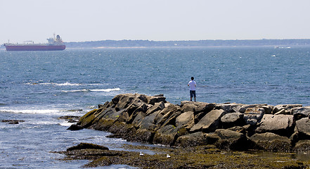 Image showing Rocky breakwater with young man and with a boat in the backgroun