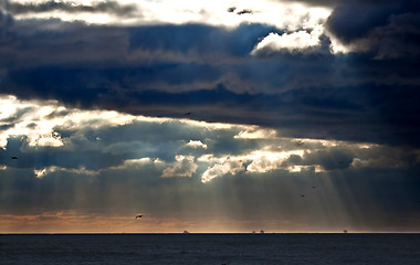 Image showing Sunbeams emanating through clouds above the ocean 