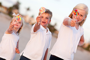 Image showing Cute Brother and Sisters Enjoying Their Lollipops Outside