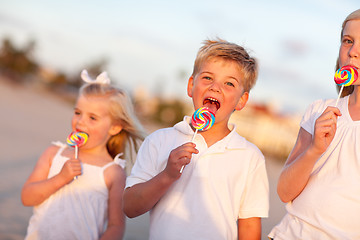 Image showing Cute Brother and Sisters Enjoying Their Lollipops Outside