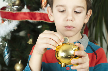 Image showing Little boy puts a coin in cash pig