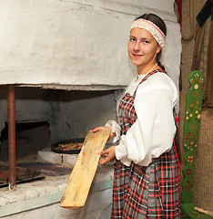 Image showing Girl in national costume prepares food on the stove