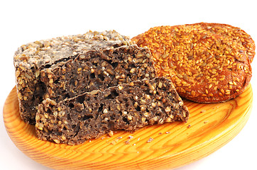 Image showing homemade brown bread and buns with sesame seeds on cutting board