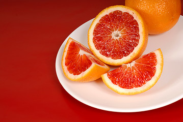 Image showing Whole and cut up blood oranges on white plate
