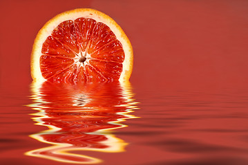 Image showing Half of a blood orange in water on a red background