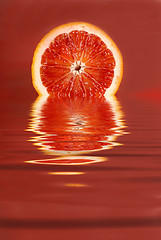Image showing Juicy half of a blood orange in water on a red background
