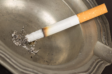 Image showing Burning cigarette in an old tin ashtray