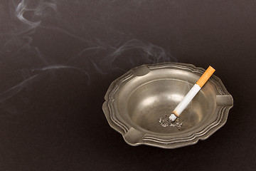 Image showing Burning cigarette in an old tin ashtray