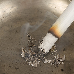 Image showing Burning cigarette in an old tin ashtray