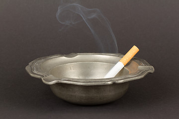 Image showing Burning cigarette in an old tin ashtray