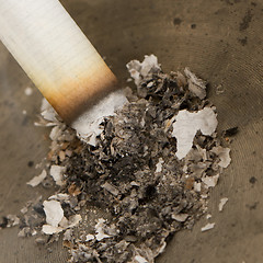 Image showing Burning cigarette in an old tin ashtray