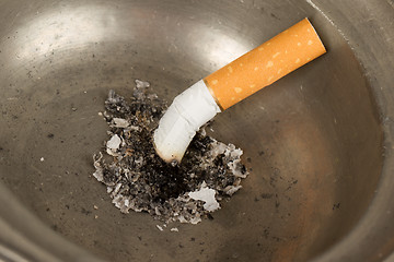 Image showing Burning cigarette in an old tin ashtray