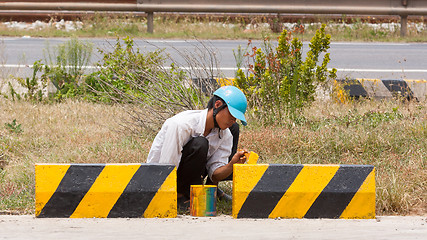 Image showing Man painting roadworks barriers on a road in Vietnam