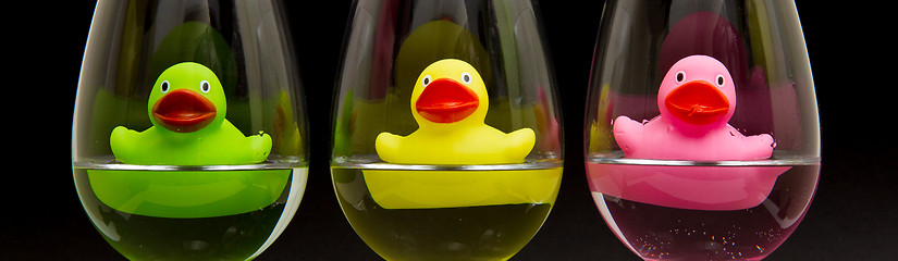 Image showing Green, yellow and pink rubber ducks in wineglasses