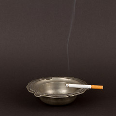 Image showing Burning cigarette in an old tin ashtray