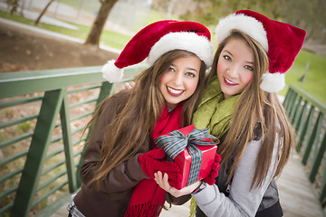 Image showing Two Smiling Women Santa Hats Holding a Wrapped Gift