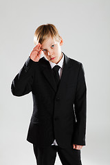 Image showing Serious young boy in black suit saluting