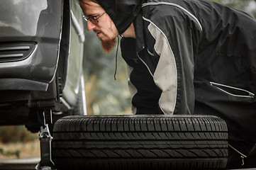 Image showing Young adult inspecting the wheel of a car