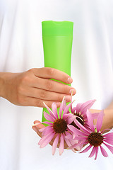 Image showing Hands of young woman holding cosmetics bottle and fresh coneflowers
