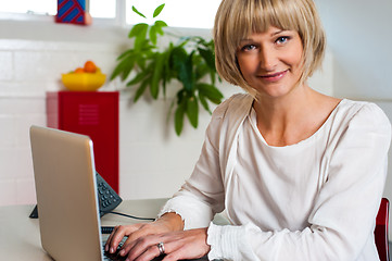 Image showing Blonde woman facing camera while working on laptop