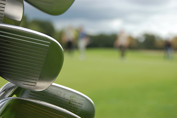 Image showing Detail of golf clubs with golfers on the green in the distance