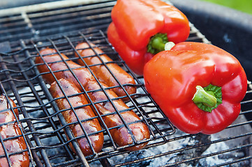 Image showing Red sweet pepper and sausages on a grill, close up