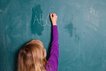 Image showing Young girl writing letters on chalkboard