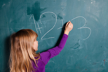 Image showing Young girl writing numbers on chalkboard