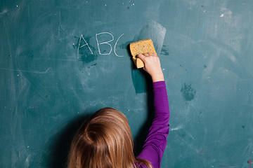 Image showing Young girl wiping chalkboard with wet sponge