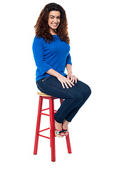 Image showing Long curly haired lady seated on red stool