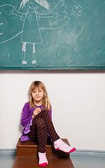 Image showing Young girl sitting in front of chalkboard