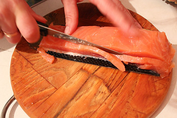 Image showing The hand cuts slices of a red fish