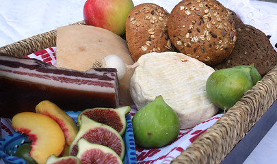 Image showing Rustic still life of bread, cheese, bacon and figs in a wicker basket