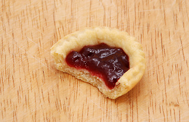 Image showing One jam tart with a bite taken, on a wooden table