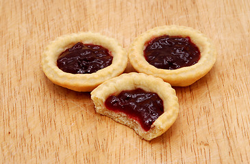 Image showing Three jam tarts, one with a bite taken, on a wooden table