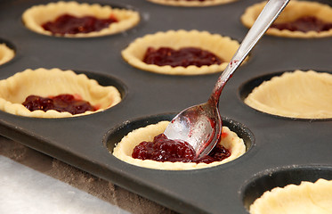 Image showing Closeup of jam tarts being filled with a teaspoon