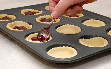 Image showing A woman's hand holding a teaspoon as she fills jam tarts