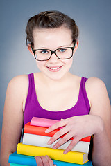 Image showing Silly smiling schoolgirl with glasses and lots of books