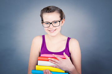 Image showing Silly smiling schoolgirl with glasses and lots of books