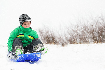 Image showing A young boy shows his excitement sledding down a hill in winter