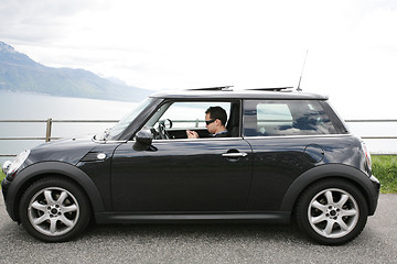 Image showing Young man in his fancy car chatting with his device up the hills