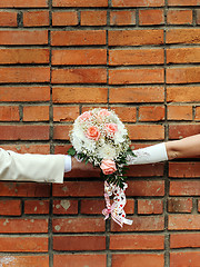 Image showing Two hands holding wedding bouquet against a brick wall.