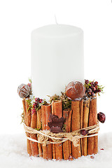 Image showing Christmas white candle in a candlestick with cinnamon and dried 