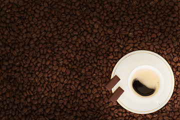 Image showing cup of coffee with chocolate pieces on coffee beans background 